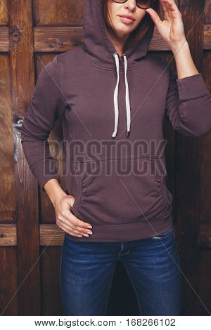 Young woman wearing blank brown sweatshirt with area for your logo or design, mock-up of template brown sweatshirt, wooden wall in the background