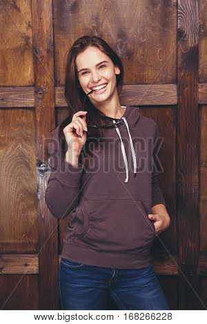 Young woman wearing blank brown sweatshirt with area for your logo or design, mock-up of template brown sweatshirt, wooden wall in the background