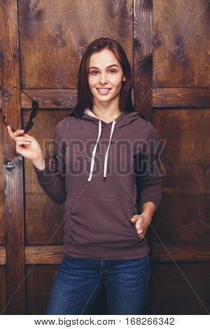 Young woman wearing blank brown sweatshirt with area for your logo or design, mock-up of template brown sweatshirt, wooden wall in the background
