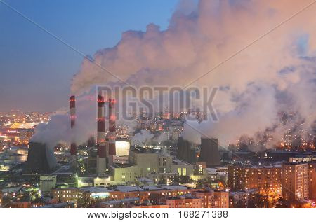 Steam and smoke from the chimneys and cooling towers city Central Heating and Power Plant. The view from the heights in the twilight winter