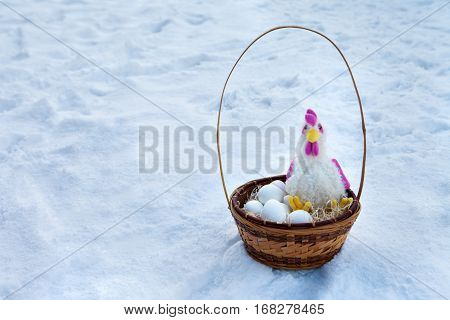 Basket with paraphernalia on Easter rooster and Easter eggs lying in basket in the snow.