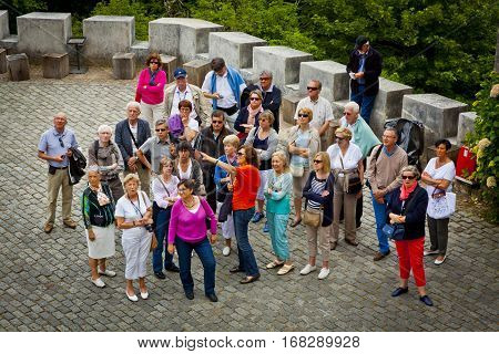 LISBON PORTUGAL - JUNE 11 2013: Group of tourists listening to the guide and looking to the building of Palace of Sintra located in the town of Sintra in Lisbon