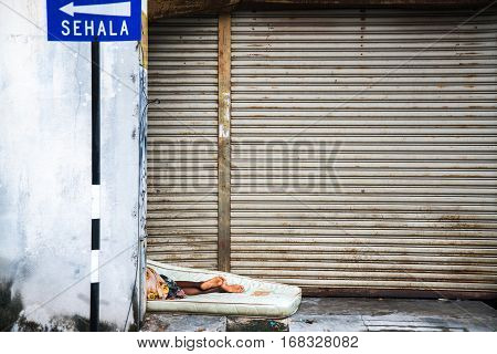 GEORGETOWN PENANG MALAYSIA - JANUARY 26 2017: Poor homeless man sleeps on the streets on a mattress. The legs in the open air lying in the street.