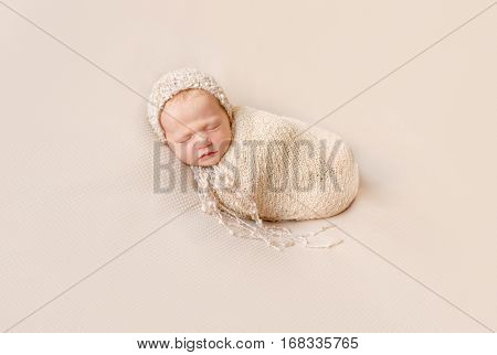 lovely wrapped newborn baby in knitted hat sleeping on a beige blanket