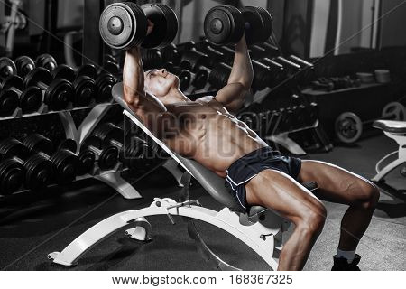Athlete muscular bodybuilder training hands with dumbbells in gym