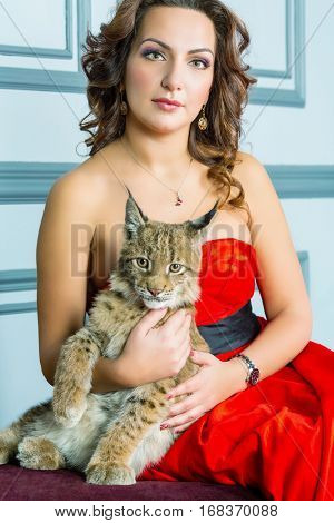 Woman in red dress sits on couch holding lynx cub.