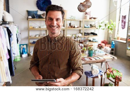 Male manager with tablet computer standing in clothes shop