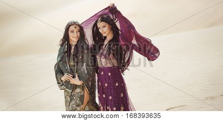 Adventure of two sisters princesses happy walking in the desert and looking at landscape. Two beautiful mixed race asian caucasianl girls enjoy a joint journey. Creative art fashion portrait shot of two gorgeous attractive models outdoors 