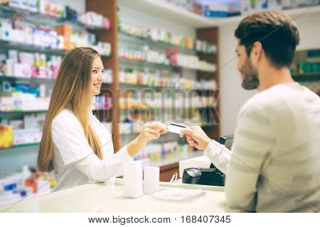 Experienced pharmacist counseling male customer in modern pharmacy and man pays with credit card