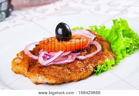 Fried beef with onion rings, tomato and lettuce leaves on white plate. Armenian food. Kofta