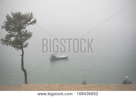 Old Man Wathing At Lonely Boat On Lake Baikal Under The Fog