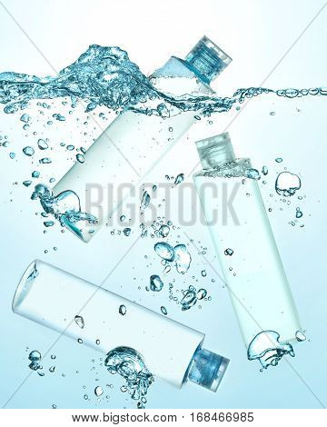 Three bottles of thermal water, cosmetic moisturizing lotion under the water. Big wave on the surface of water and many big and small bubbles in the water. Gradient blue background