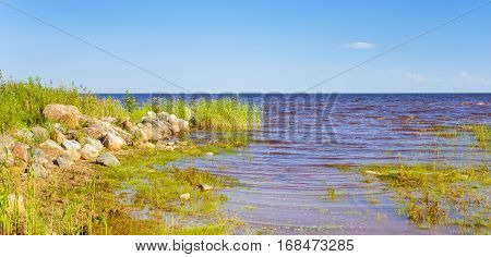 Shore of lake Peipsi in Eastern Estonia. Chudskoye is large freshwater lake with rich history where occurred famous battle of Ice. Huge granite stones among grass & reeds near water. Fishing village
