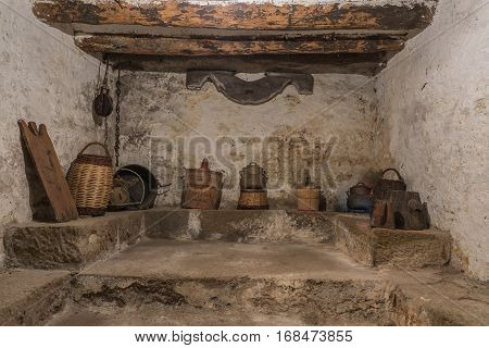 Basement of an old house with wooden beams and wall with humidity, antique household items, carboy demijohn, stewpot, plank, Wicker basket, pulley with chain, yuguillo
