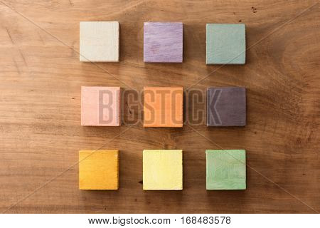 Index, menu or cover abstract back ground, consisting of nine hand painted colored wooden cubes on grungy wooden background with vintage taste.  warm neutral colors. orange, gray, green, beige, pink.