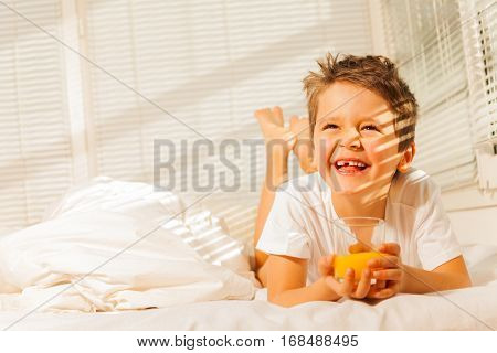 Portrait of smiling boy laying in his bed with glass of fresh orange juice