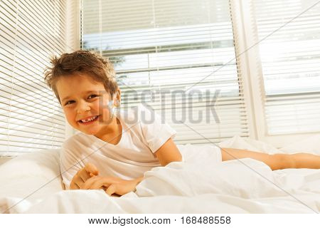Portrait of cute kid boy smiling while lying on his bed in the morning
