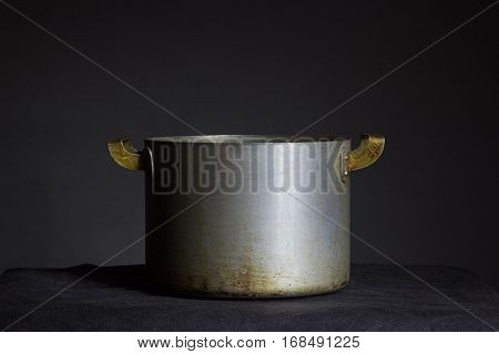 Belarus Minsk - Old metal pot with handles on a black background placed on a table covered with a black cloth pot is made in the USSR scorched in the fire pan.