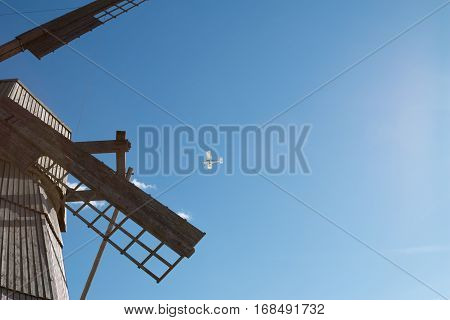 Belarus Dudutki - A small white airplane flying over the old wooden mill in Dudutki a large and old mill wants to break a small plane in a blue sky.