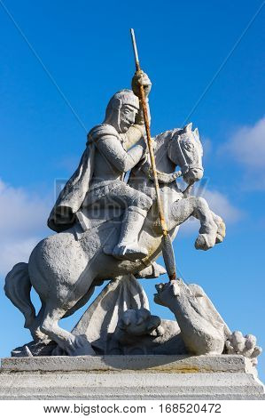 Orkneys Scotland - June 5 2012: Closeup of white concrete statue of Saint George sitting on horse defeating a dragon against deep blue sky. Outside the Italian Chapel on Lamb Holm Island. Rusty spear.