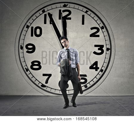 Businessman waling hme exhaustedly with a clock n the background
