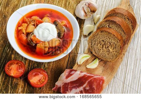 Red vegetable soup in the white plate and bread. On a wooden background.