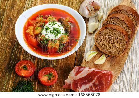 Red vegetable soup in the white plate and bread. On a wooden background.