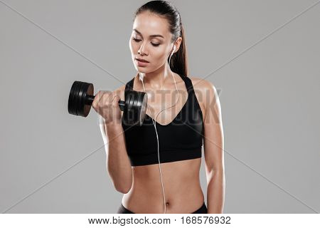 Pretty Sporting woman using dumbbell in studio. Isolated gray background