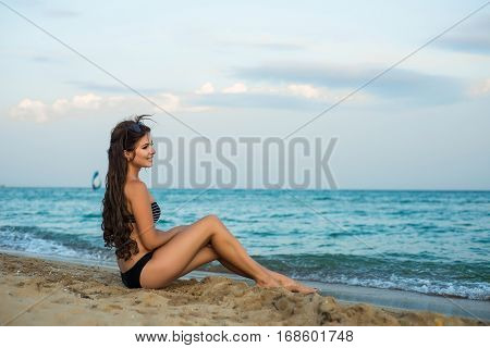 The girl brunette sits on the beach in the evening
