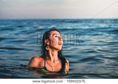 Beautiful young brunette woman in the sea at sunset