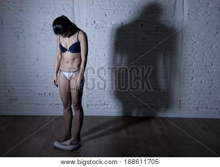young fit and slim woman or teenager girl checking body weight on scale with big edgy shadow light sad desperate and frustrated in anorexia and bulimia nutrition disorder and overweigh obsession
