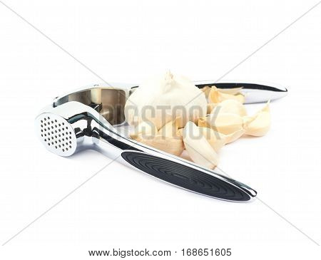 Metal garlic press utensil next to a pile of fresh cloves isolated over the white background