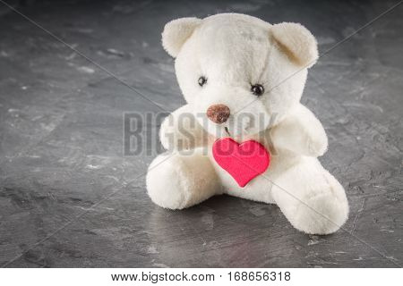 White teddy bear with love letter on red heart on gray background. Say i love you for valentine 's day concept.