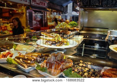 BARCELONA SPAIN - MAY 2016: Fried Gould's razor shell or Canyut navaja in olive oil and pesto. Shrimps bamboo jack knife clams and mussels on ice in glass case of cafe at Mercat de Boqueria market
