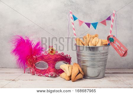 Jewish Purim holiday concept with hamantaschen cookies or hamans ears in bucket and carnival mask over rustic background