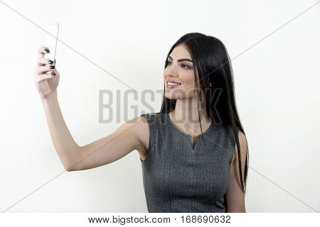 Young business woman using her smart phone to shoot a selfie and smiling.