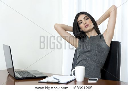 Young business woman with her hands behind her neck looking tired at her office.