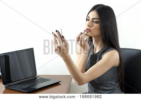 Business woman puts lipstick and using her phone as a mirror.