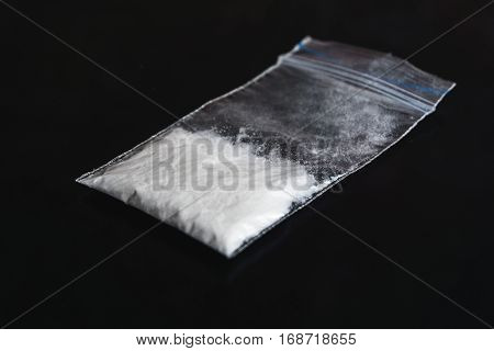 Cocaine in plastic packet on black background, closeup. Portion of drugs
