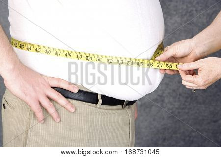 Woman measuring waist of overweight  man with tape measure, middle section