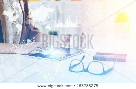 Close up of a woman sitting in office and using her tablet computer. There are graphs and a world map on the foreground. Toned image. Double exposure