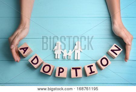 Female hands, cubes with word ADOPTION and figure in shape of happy family on wooden background