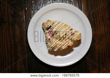 Cranberry scone on a white ceramic plate on a wooden table in a coffee shop