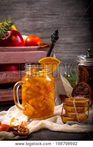 Bank of orange jam on a wooden background in the background a box of fruit and the Bank with candied fruit