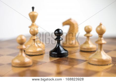 Black pawn surrounded by white chess pieces on a chess board