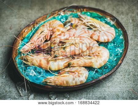 Raw uncooked tiger prawns on chipped ice in turquoise blue tray over grey concrete background, selective focus, horizontal composition. Fresh seafood concept