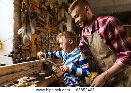 family, carpentry, woodwork and people concept - happy father and little son with rasp grinding wood plank at workshop