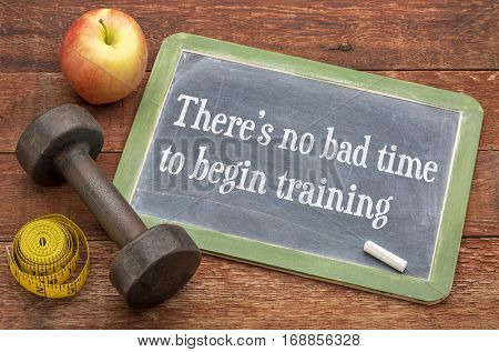 There is no bad time to begin training -  slate blackboard sign against weathered red painted barn wood with a dumbbell, apple and tape measure