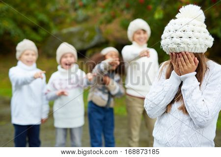 Crying girl hiding her face while classmates bullying her