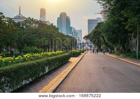 Business district cityscape from a Lumpini park with people walking at a sunset time in Bangkok, Thailand. Outdoor evening landscape with green park nature and skyscrapers on horizon at twilight, Asia